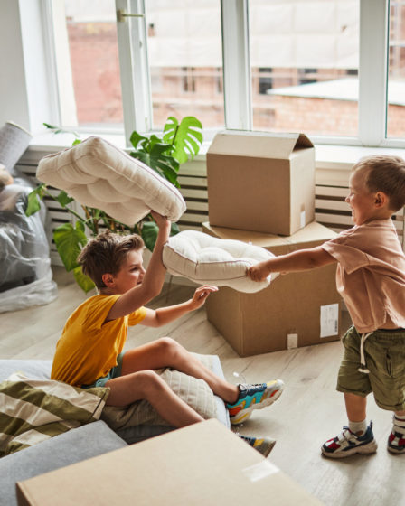 Children playing pillow fight in new home, moving boxes and home decor in background.