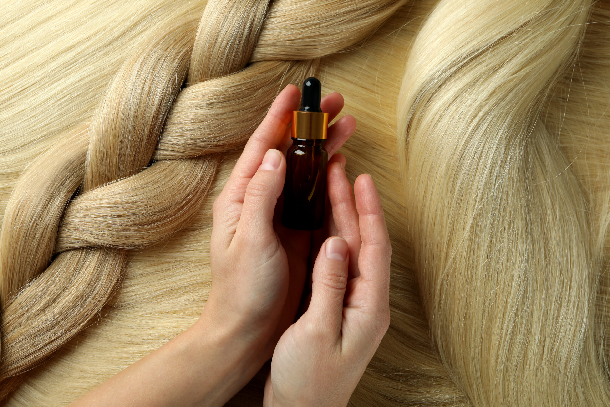 Female hands holding bottle of hair care product with braided blonde hair