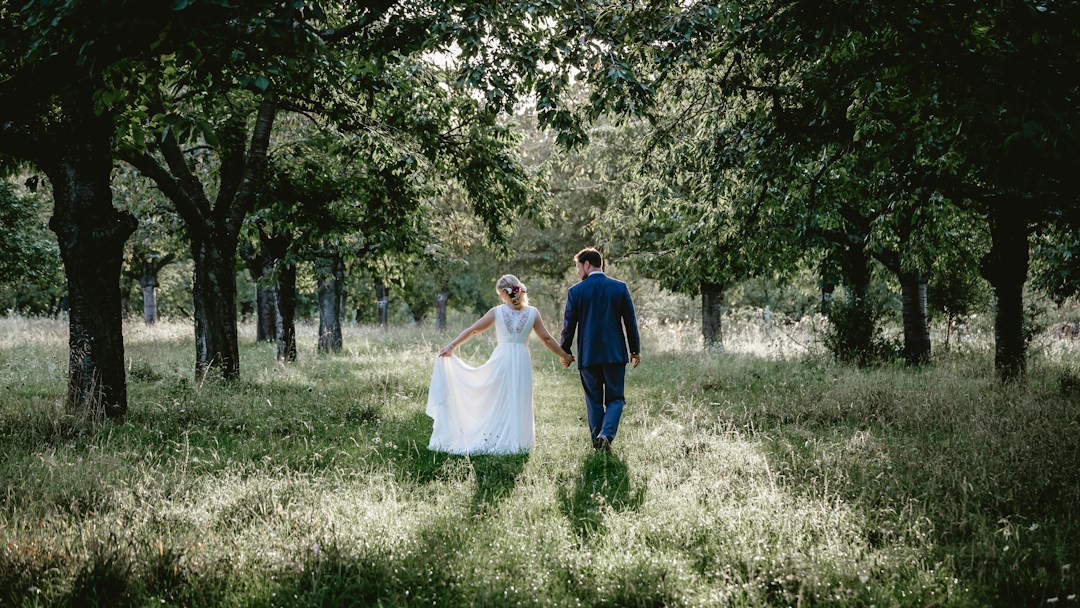 Bride and groom walking hand-in-hand through a sunlit forest, romantic wedding photography backdrop.